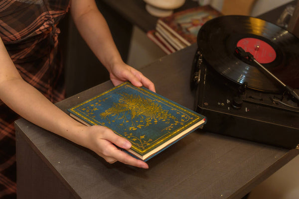 Person holding a decorative book next to a vinyl record player with a red label.