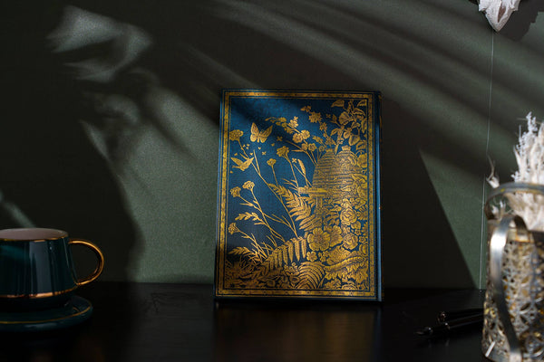 Decorative book with gold illustrations on a dark surface with a green wall background