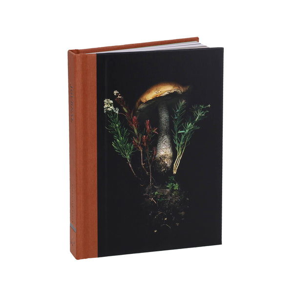 Book with a brown spine and black cover featuring a mushroom and plants design on a white background